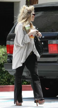 a woman walking down the street with her hand in her pocket and holding a coffee cup