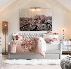 a white bed with pink comforter and pillows in a room that has lights on the ceiling