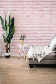 a living room with pink brick wall and wooden flooring next to a gray couch