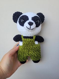 a hand holding a small crocheted panda bear in green overalls with black and white stripes