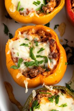 three stuffed peppers with meat and cheese in them on a white plate next to other vegetables