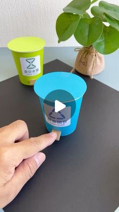 a hand is holding an ice cream container on a table next to a potted plant