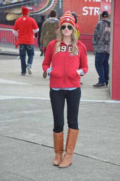 a woman standing on the sidewalk wearing boots and a red jacket with numbers on it