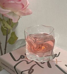 a pink rose sitting on top of a book next to a glass filled with water