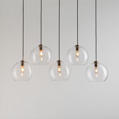 five clear glass globe pendant lights hanging from black cords against a white wall, with one light turned on