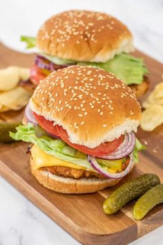 two hamburgers on a cutting board with pickles