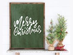 a green christmas sign sitting on top of a shelf next to a potted plant