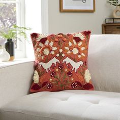 a decorative pillow on a white couch in a living room with a window and potted plant