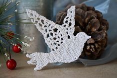 a white crocheted bird sitting next to a pine cone