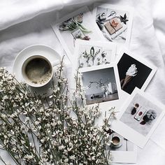 flowers and photographs on a white sheet next to a cup of coffee