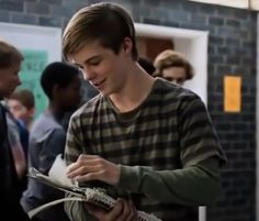 a young man holding a guitar while standing next to other people in a room with brick walls