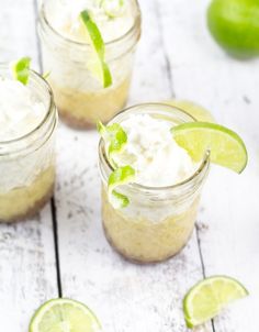 three small mason jars filled with whipped cream and limes on a white wooden table