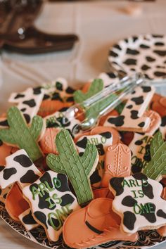 decorated cookies are arranged on a plate at a party or event, with cactus and cow theme