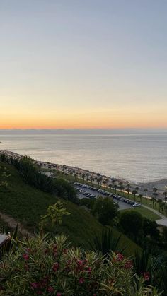 the sun is setting over an ocean and beach with cars parked on the shore line