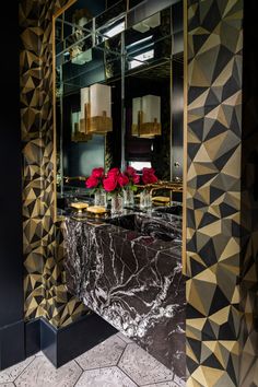 a black and gold bathroom with roses in vases on the counter top, mirror behind it