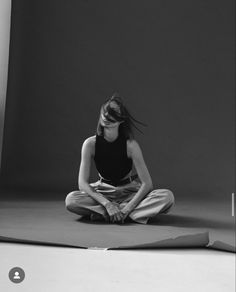 a woman sitting on the floor in front of a black and white background with her hands crossed