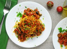 two white plates topped with spaghetti and tomato sauce next to silverware on a table