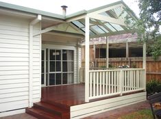 a white house with a wooden deck in the front yard and covered patio area next to it