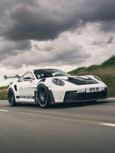 a white sports car driving down the road under dark clouds and rainclouds