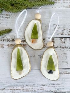 three ornaments with green trees on them hanging from the side of a white wooden table