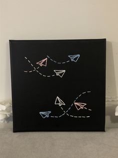 a black canvas with white and pink paper airplanes flying in the sky on it's side