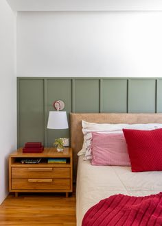 a bed with red and white pillows on top of it next to a night stand