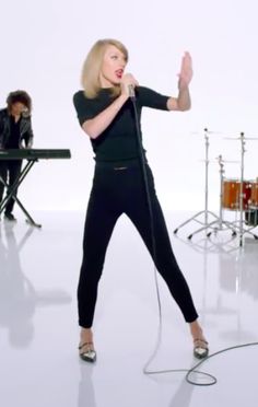 a woman is singing into a microphone in front of drummers and drum set behind her