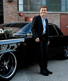 a man in a suit leaning on the hood of a black car with an engine