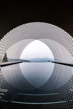 the reflection of trees in the water is shown through a circular structure that looks like it has been made out of metal mesh