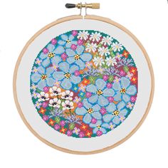 a cross stitch pattern with blue flowers in the center on a white wall hanging from a wooden hoop