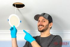 a man wearing blue gloves is holding up a light fixture and pointing to the ceiling