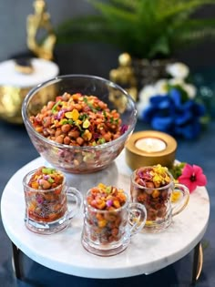 a table topped with two cups filled with food next to a bowl full of beans