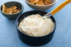 two bowls filled with dip and crackers on top of a blue tablecloth next to each other