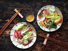 two white plates topped with salad and chopsticks next to each other on a wooden table