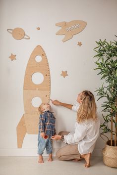 a mother and her son are playing with a wooden rocket ship wall decal in their nursery