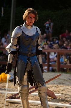 a man dressed as a knight standing on top of a sandy field next to a crowd