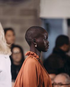 a model walks down the runway in an orange top and white pants with her hair pulled back