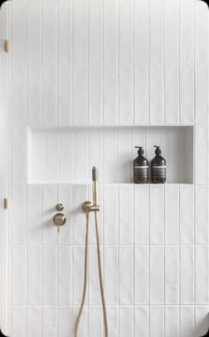 a white tiled bathroom with two soap dispensers on the wall and a shower head