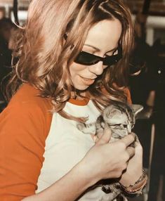 a woman holding a cat in her arms and wearing sunglasses on top of her head