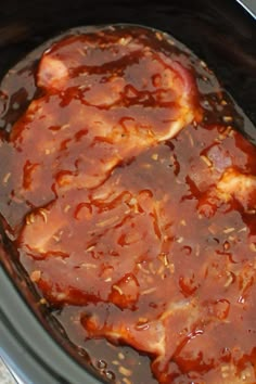 a slow cooker filled with meat covered in bbq sauce and seasoning sprinkled on top