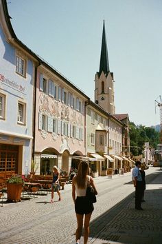 a woman walking down the street in front of buildings with a clock tower on top