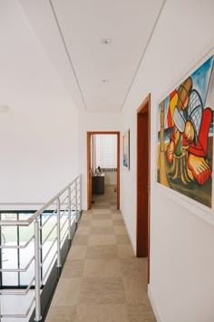 an empty hallway with paintings on the wall and stairs leading to another room in the background