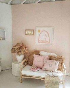 a white couch with pink pillows on top of it next to a basket and plant