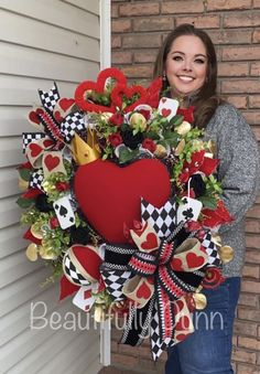 a woman standing in front of a door holding a heart wreath with playing cards on it