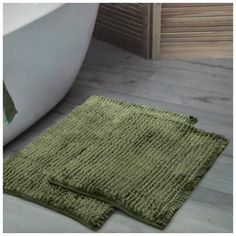 two green rugs sitting on the floor next to a bath tub