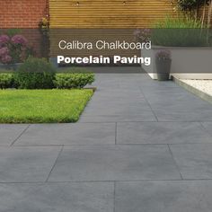 a sidewalk with grass and flowers in front of a brick building that says porcelain paving