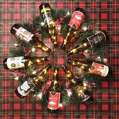 a christmas wreath made out of beer bottles on a plaid tablecloth with lights around it