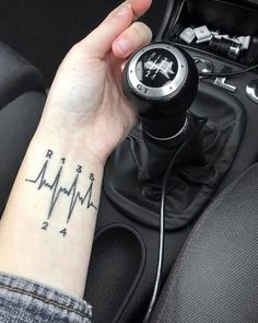 a person with a tattoo on their arm holding a car steering wheel knob and an electronic device