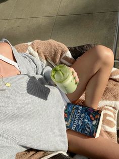 a person laying on a towel with a book and a cup in their hand while holding a drink