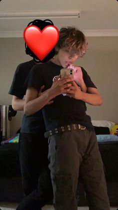 two people standing next to each other looking at a cell phone with a heart on the screen